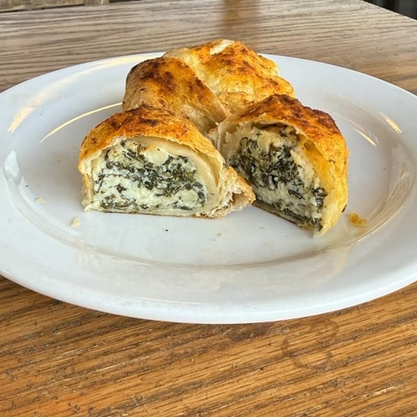 Golden-brown spinach and feta pastries, one cut open to show the creamy filling, on a white plate.