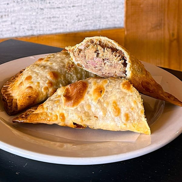Three golden-brown empanadas on a white plate, one cut open revealing a savory meat filling.