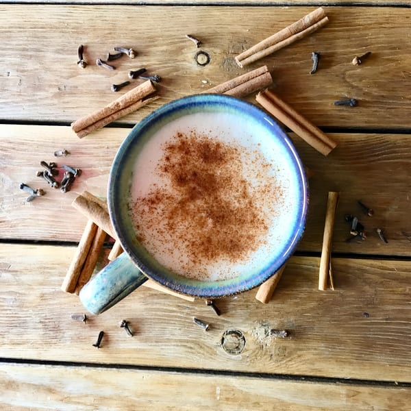 Overhead view of a World Blend Coffee latte with cinnamon, surrounded by cinnamon sticks and cloves.