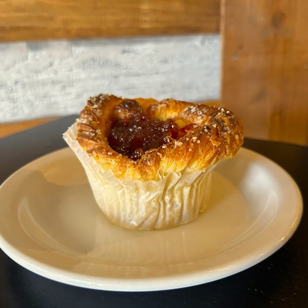 A golden-brown pastry with a dark fruit filling and sugar sprinkles, served on a white plate.
