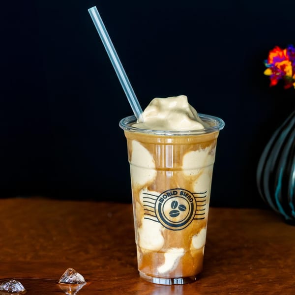 A World Blend coffee frappe with a straw, ice cream, and coffee swirls on a wooden table.